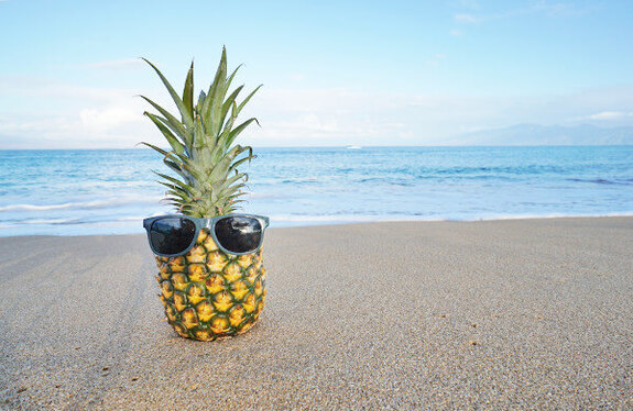 Humorous pineapple with sunglasses on sandy beach